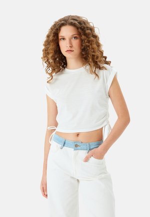 Hvid cropped t-shirt med rullede ærmer og drawstring i siderne, parret med høj talje hvide jeans og et lysblåt denimbælte.