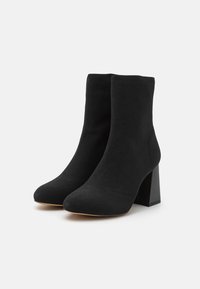 Botines negros de tobillo hechos de tela suave, con punta afilada y un tacón bloque grueso para mayor estabilidad. Superficie lisa sin acentos visibles.