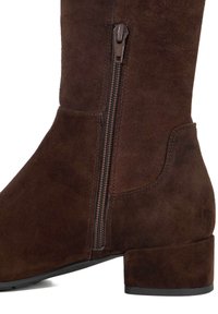 Brown suede knee-high boot featuring a side zipper, cylindrical heel, and smooth texture. Sleek, fitted design with minimal accents.
