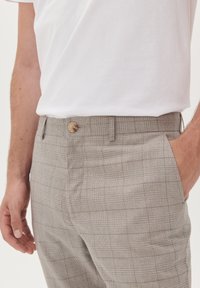 Beige karierte Hose mit Knopfverschluss, seitlichen Taschen und lockerer Passform, aus leichtem Stoff für Komfort gefertigt.