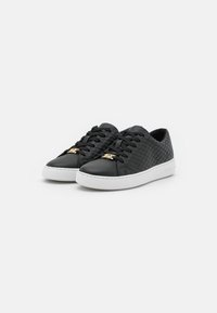 Schwarze, geflochtene Leder-Sneaker mit weißen Sohlen und goldenen Schnürsenkeltags, nebeneinander auf einem weißen Hintergrund gezeigt.