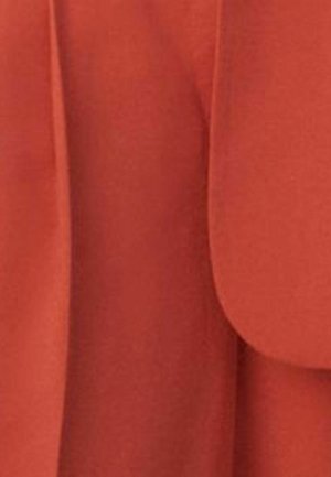 Prim-plan cu o țesătură portocaliu-ruginie cu margini ascuțite și pliuri subtile, cel mai probabil parte a unui articol de îmbrăcăminte sau tapițerie.