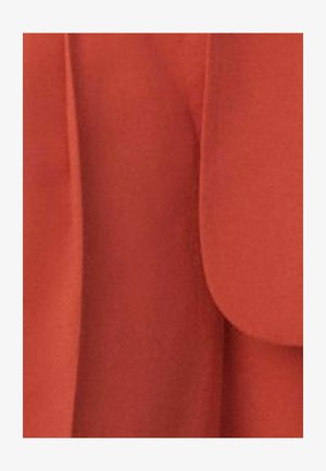 Lähikuva ruosteenoranssista kankaasta, jossa on terävät reunat ja hienovaraiset taitteet, todennäköisesti osa vaatetta tai verhoilua.