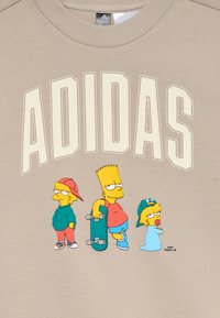 Beige sweatshirt featuring "ADIDAS" in cream letters, and cartoon characters from *The Simpsons*: Bart with a skateboard, Lisa, and Maggie.