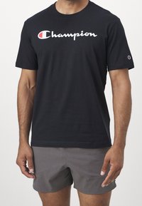 Černé bavlněné tričko s bílým logem "Champion" přes hruď. Krátké rukávy, kulatý výstřih, s malým logem na rukávu.