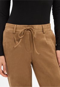 Helle Wildledershorts mit Zugband-Taille, die Seitentaschen und eine glatte Textur aufweisen. Mit dezenten Falten vorne.