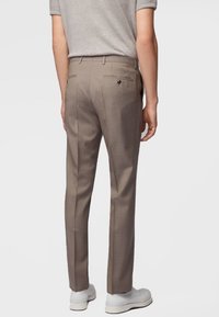 Brązowe, dopasowane spodnie o wąskim kroju, z tylnymi kieszeniami i gładką fakturą, zestawione z białymi trampkami dla casualowego wyglądu.