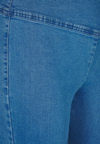 Sininen denim-kangas, jolla on sileä pinta, esittelee lähikuvan ompelusta ja vaatteen muodosta. Sisältää klassisen muotoilun.