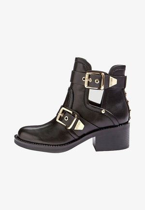 Bottine noire en cuir avec quincaillerie dorée, deux accents de boucles, tige texturée et talon bloc. Dispose d'un détail de découpe sur le côté.