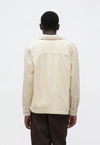 Bézs kordbársony ing hosszú ujjakkal, bordázott textúrával, gombos mandzsettákkal és hátsó yoke részlettel. A dizájn klasszikus gallért tartalmaz.