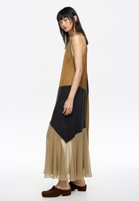 Maxi sukienka w brązowym, czarnym i beżowym kolorze. Posiada lejącą się dolną część z szyfonu, górę z jednolitego materiału z regulowanymi ramiączkami oraz luźny krój.
