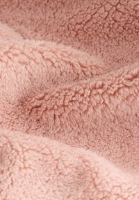 Měkká růžová fleece tkanina s nadýchanou strukturou, která má kudrnatá vlákna vytvářející hloubku a rozměr v pokrčeném uspořádání.