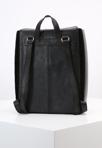 Svart läderryggsäck med två justerbara remmar, ett handtag på toppen och en minimalistisk design med subtila sömnadsdetaljer.