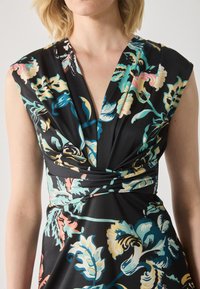 Robe florale noire avec un décolleté en V profond, des manches courtes et une taille cintrée. Le tissu est lisse avec des motifs floraux vibrants en bleu, rose et vert.
