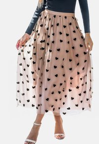 Een beige tule rok met zwarte hartpatronen, met een aansluitende tailleband en een vloeiende silhouette, gecombineerd met witte sandalen met banden.