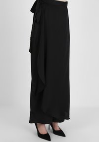 Svart omslagspåse gjord av lätt tyg med en sidband, har en flytande siluett och en fåll som hänger elegant.
