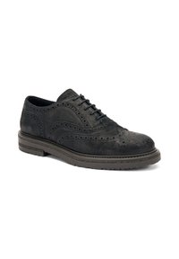 Scarpa brogue nera in suede con dettagli intricati e suola in gomma spessa, angolata per mostrare il design e la texture.