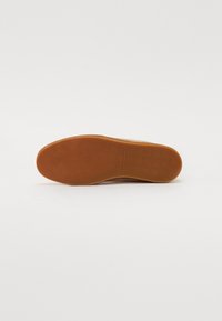 Semelle en caoutchouc brun clair d'une basket avec de fins motifs circulaires et le marquage « Karl Lagerfeld » au centre.