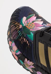 Zapatilla con un upper de punto azul marino que presenta vibrantes bordados florales en rosa, verde y naranja. Suela de goma negra con acentos florales.