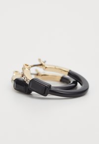 Une paire de boucles d'oreilles créoles en or avec des accents de pierre noire rectangulaire et de petites cristaux transparents sur un fond blanc.