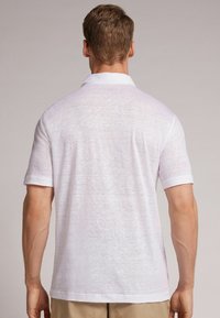 Bílá polo košile s krátkým rukávem vyrobená z lehkého materiálu, s klasickým límcem a ohrnutými rukávy, s jemnou texturou.