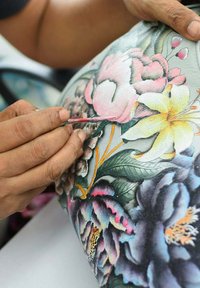 Handbeschildering op leer met kleurrijke bloemen, waaronder roze pioenrozen en gele lelies, met complexe groene bladeren en gedetailleerde schaduwen.