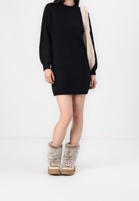 Robe tricotée noire à manches longues, associée à des bottes beige doublées de fourrure avec une semelle en caoutchouc. Texture douce et design simple.