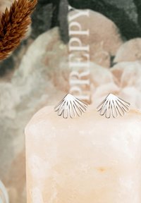 Silverörhängen i en fläktform med avlånga, rundade sektioner. Visas på en ljus stenhäll med en slät textur.