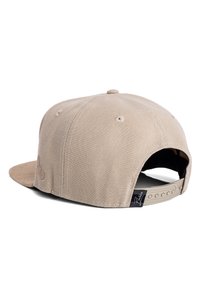 Beige snapback sapka texturált vászon anyagból, lapos karimával és puha velúr alsó karimával. Az oldalán fekete márkacímke található.