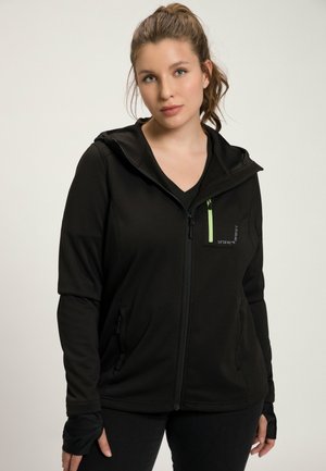 Veste noire zippée en matériau lisse et extensible, avec une capuche, une poche d'accent vert et des ouvertures pour les pouces sur les manches.