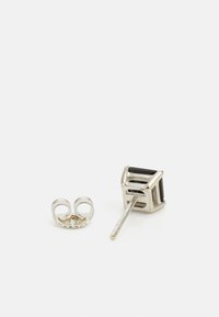Orecchini in argento con un design cubico e una pietra nera, accompagnati da un accento ad anello curvo. La superficie è lucida e testurizzata.