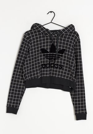Sweat à capuche court noir avec des lignes de grille blanches, logo Adidas au centre, cordons sur la capuche, suspendu sur un cintre noir sur fond blanc.