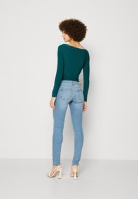 Teal langermet topp med bred hals, kombinert med lyseblå skinny jeans og hvite høyhælte sandaler. Glatt stoff og tettsittende design.