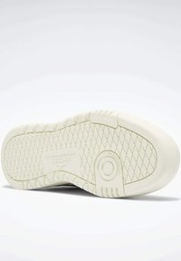 White rubber shoe sole with diamond traction pattern. Features a circular padded area, "Reebok" logo, and textured sections along the edges.