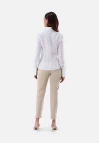 Camicia bianca di lino a maniche lunghe con polsini a bottoni, abbinata a pantaloni beige, indossata con sandali con tacco chiari, vista da dietro.