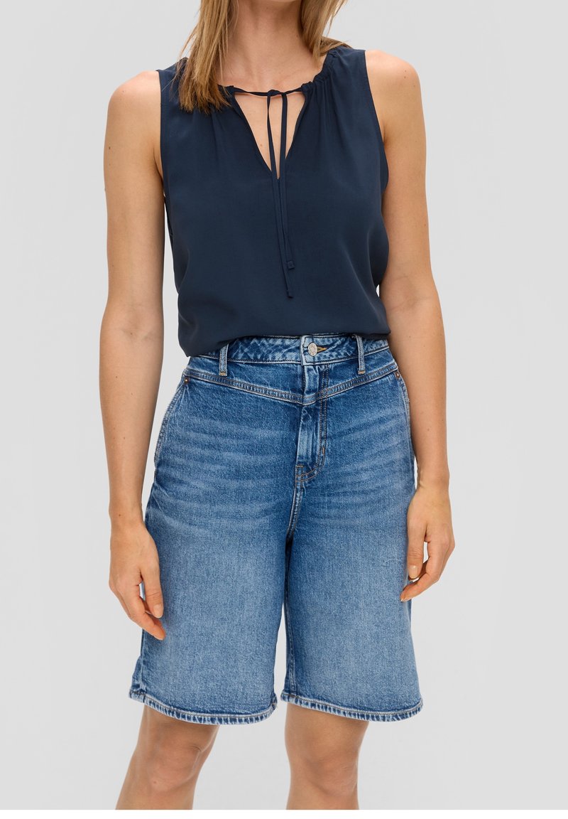 Blouse sans manches bleu marine avec un col en trou de serrure et un détail à nouer, associée à un short en jean taille haute avec un lavage clair et un ourlet effiloché.