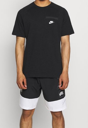 Homme portant un T-shirt noir Nike avec un logo blanc sur la poitrine et un short noir et blanc avec des patchs et un swoosh Nike sur la jambe.