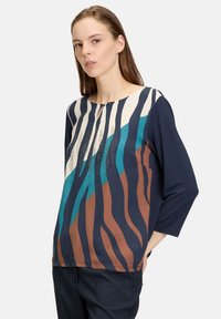 Mångfärgad långärmad skjorta med abstrakta ränder i marinblått, brunt och teal, med rund halsringning och dekorativa nitar.