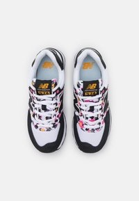 Baskets noir et blanc avec un motif floral multicolore sur les lacets, présentant un design en daim et mesh. Logo New Balance affiché.