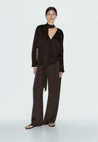Haut marron foncé, avec une texture satinée et un détail de foulard noué. Assorti à un pantalon ample. Design minimaliste et texture lisse.