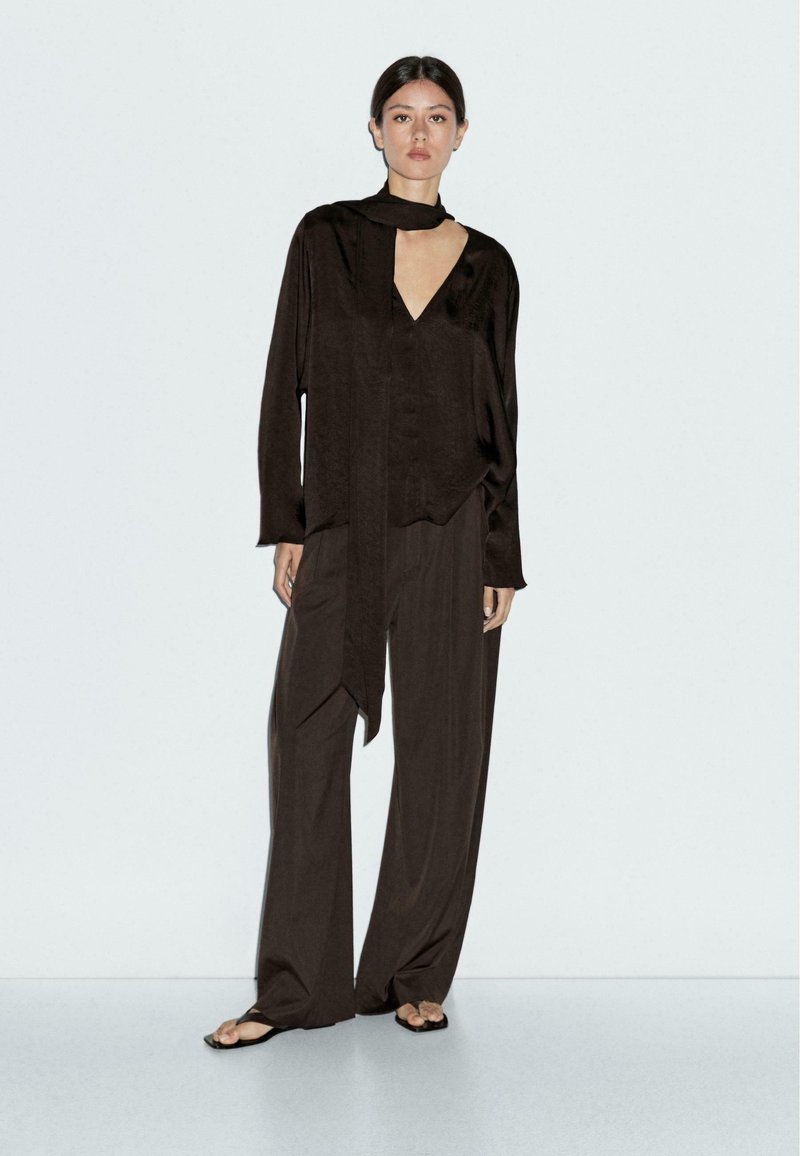Haut marron foncé, avec une texture satinée et un détail de foulard noué. Assorti à un pantalon ample. Design minimaliste et texture lisse.