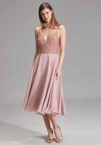 Blush roze jurk met een bedazzeld lijfje en V-hals; vloeiende chiffon rok; dunne bandjes; metalen zilveren haksandalen.