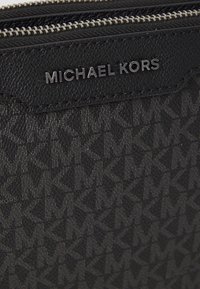 Black leather wallet with embossed 'MK' pattern, silver zipper hardware, and a metal brand logo. Textured surface with a sleek design.
