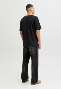 Sort bomulds-T-shirt med afslappet pasform, kombineret med løstsiddende, falmede sorte jeans. Outfit'et inkluderer tanfarvede slip-on sko.