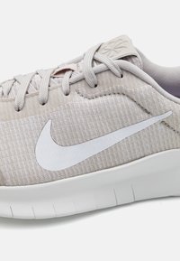 Vaaleanbeige urheilukengät, joissa on teksturoitu kangaspinta, valkoinen Nike-logo ja kontrastivalkoinen pohja, jossa on vaakasuorat urat pitävän otteen takaamiseksi.
