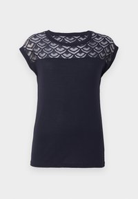 Mörkblå t-shirt med en texturerad spetsaxel i en scalloped-mönster, korta cap ärmar och rund halsringning. Slät bomullstyg.