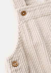 Close-up of light beige corduroy fabric with vertical ridges and two small brown four-hole buttons attached.