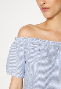 Top azul claro e branco com riscas, com decote ombro a ombro, mangas curtas bufantes e tecido texturizado; possui um decote com babados.