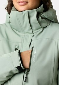 Light green waterproof jacket featuring a high collar, zippered pockets, and adjustable cuffs with a velcro strap. Branding on the front.