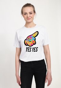 Hvid bomulds t-shirt med et farverigt, abstrakt hånd, der peger til højre, og teksten "YES YES" i fede sorte bogstaver nedenfor.